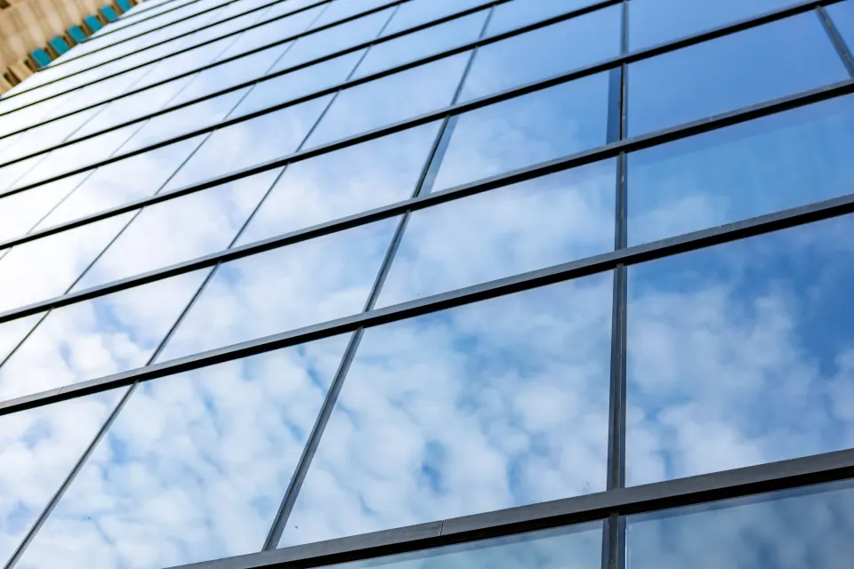 Glasfassade eines Bürogebäudes mit Spiegelfolie und Himmelspiegelung bei blauem Himmel
